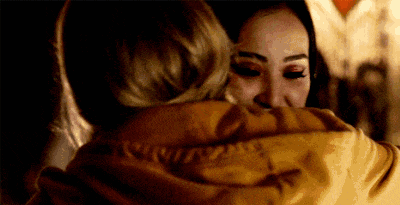 two women are hugging each other in a dark room . one of the women is wearing a yellow jacket .
