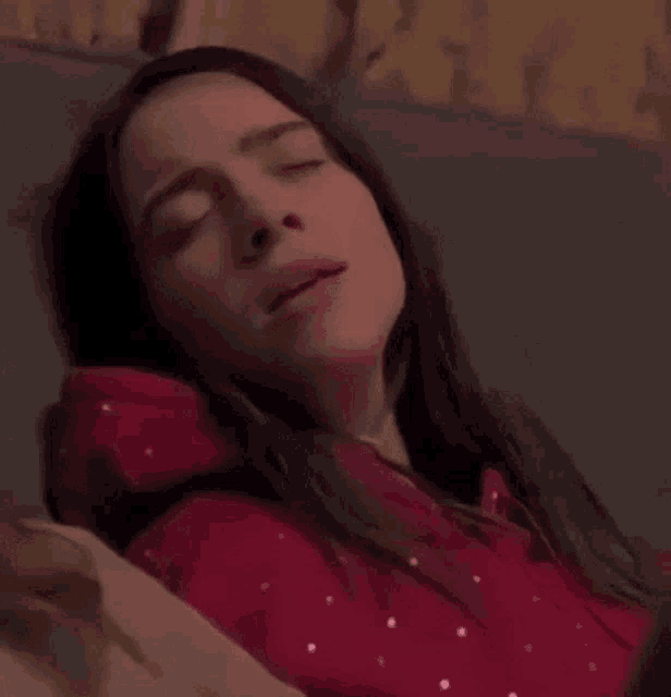 billie eilish is laying on a bed with her eyes closed and looking at the camera .