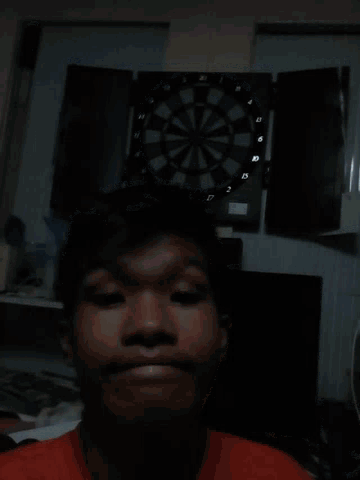 a man is smiling in front of a dart board with the numbers 1 to 12 on it