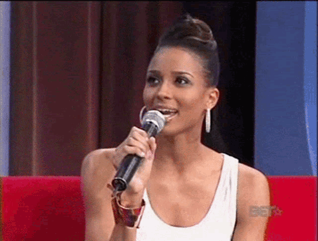 a woman in a white tank top is holding a microphone in front of a screen that says bet