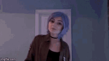 a woman with purple hair and a choker is wearing a brown jacket and a black top .