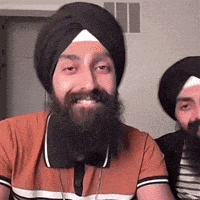 a man with a beard wearing a turban is smiling next to another man .