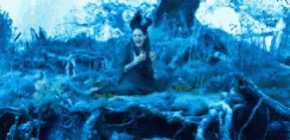 a woman in a black dress is sitting on a rock in a blue forest .