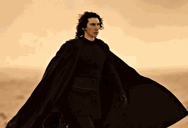 a man in a black cape is walking across a desert