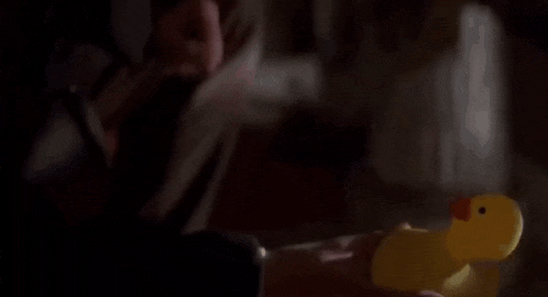 a person is holding a yellow rubber duck with a red beak on a wooden floor .