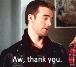 a man in a leather jacket is standing in front of a wall and saying aw , thank you .