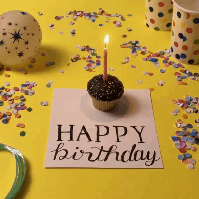 a cupcake with a lit candle on top of a happy birthday card