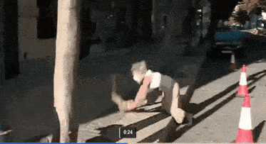 a man is kneeling down on a sidewalk with a video playing at 0.24