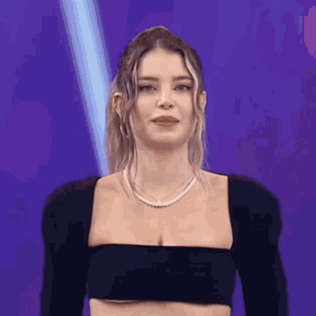 a woman wearing a black crop top and a pearl necklace is standing on a stage .