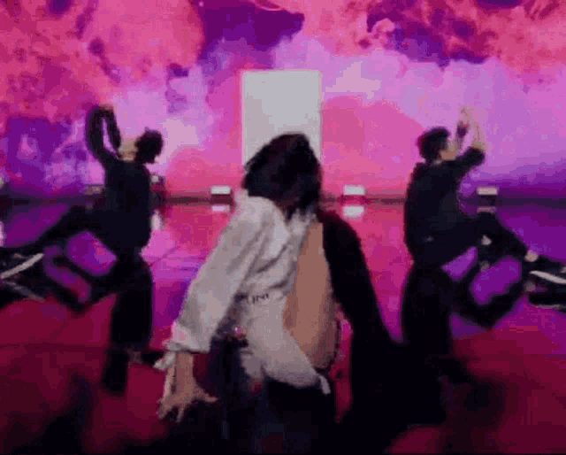 a group of dancers are dancing on a stage in front of a purple background .