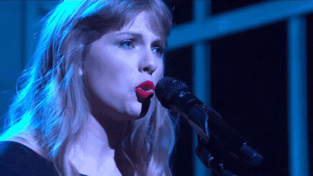a woman singing into a microphone with red lipstick on her lips