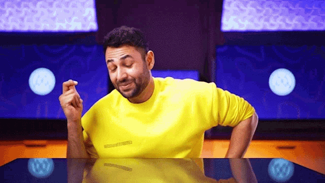 a man in a yellow shirt is sitting at a table with his hands on his knees .