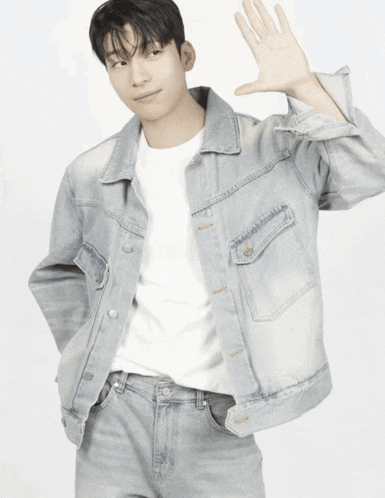 a young man wearing a denim jacket and jeans is waving