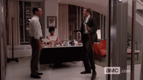 three men are standing in a room with a sign that says ' a.m.c.com '