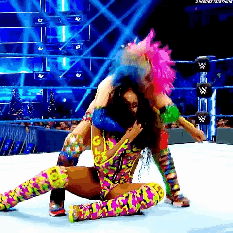 a woman with pink hair is wrestling another woman in a ring .
