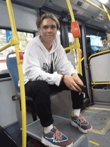 a young man sitting on a bus wearing a white hoodie with the letter dn on it