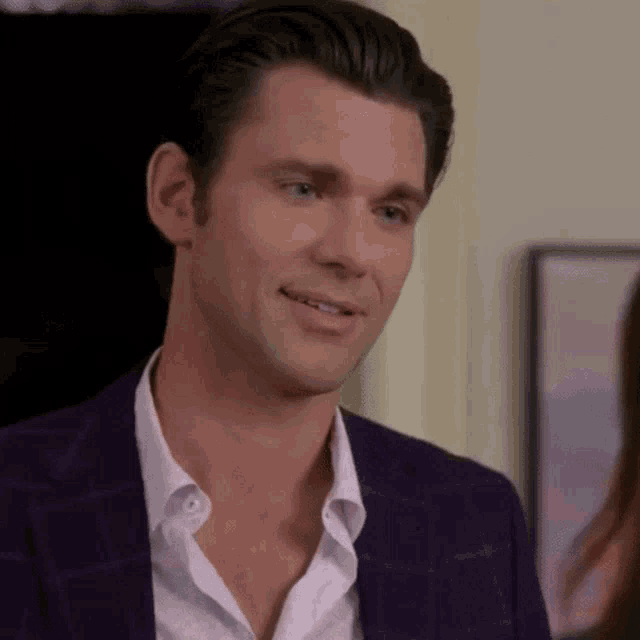 a man in a purple suit and white shirt is smiling and talking to a woman .