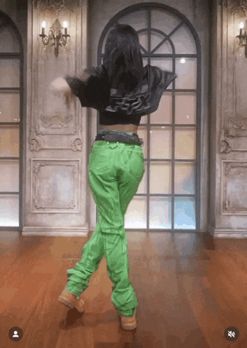 a woman wearing green pants and a black jacket is dancing
