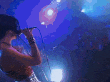 a woman sings into a microphone with a crowd behind her