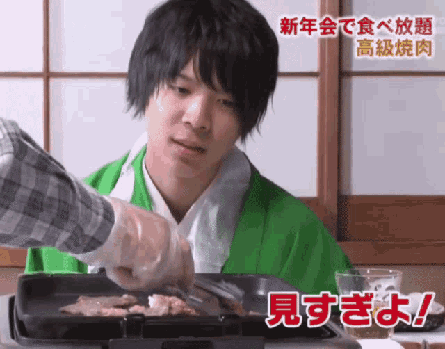 a man in a green jacket is cooking food on a grill with chinese writing behind him