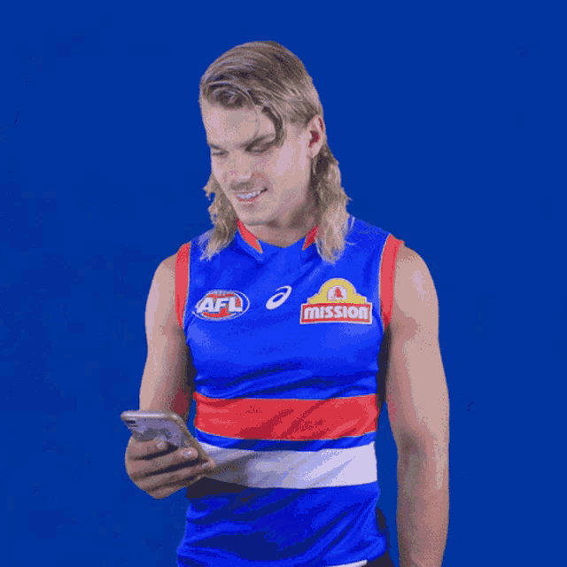 a man wearing an afl jersey looks at a cell phone