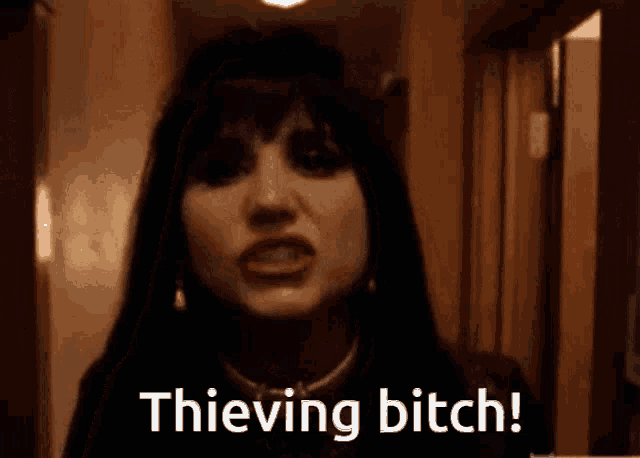 a woman is standing in a hallway with the words " thieving bitch " written on her face .
