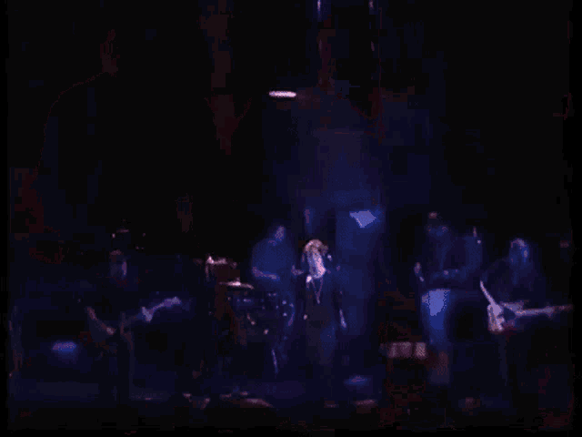 a woman is singing into a microphone on a stage while a man plays drums in the background .