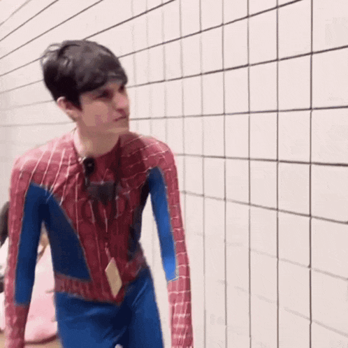 a man in a spiderman costume is standing in front of a white tiled wall