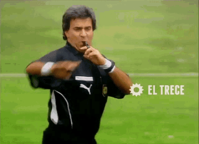 a man is blowing a whistle on a field with el trece in the corner