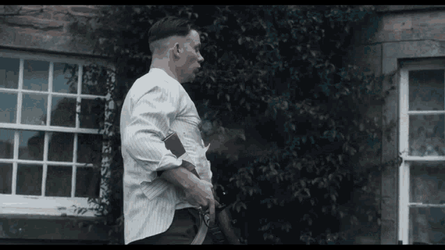 a man in a striped shirt is standing in front of a window holding a gun .