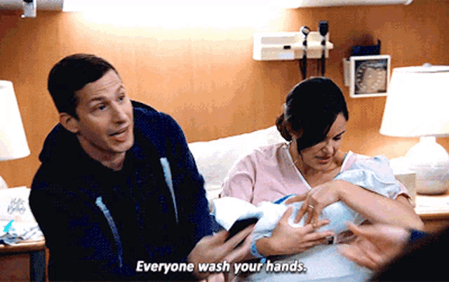 a man and a woman are holding a baby in a hospital room and the man says everyone wash your hands
