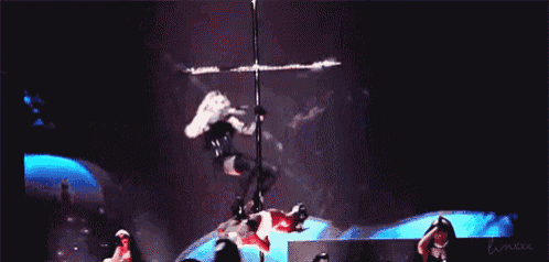 a woman is hanging from a pole on a stage with a cross behind her .