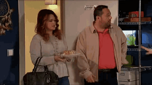 a man in a red shirt is standing next to a woman holding a plate