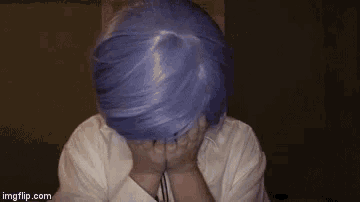 a woman with purple hair is covering her face with her hands .