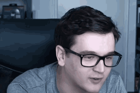 a man wearing glasses is sitting in a chair and making a funny face .