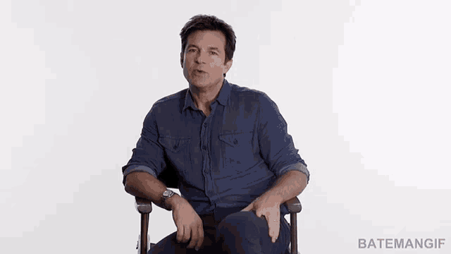 a man in a blue shirt is sitting in a chair with the word batemangif on the bottom