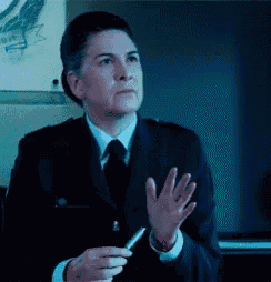 a woman in a suit and tie is holding a pen and waving her hand .