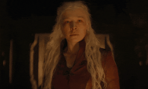 a woman with white hair and a red jacket looks at the camera