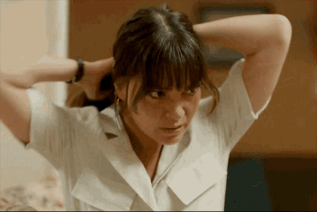a woman in a white shirt adjusts her hair