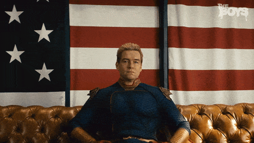 a man in a superhero costume sits on a couch in front of an american flag with the boys written on the bottom