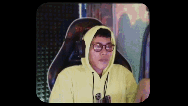 a man wearing glasses and a yellow hoodie is sitting in a chair