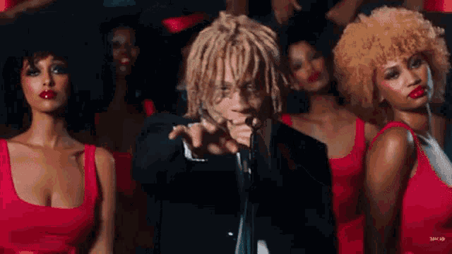 a man in a suit is singing into a microphone in front of a group of women in red dresses