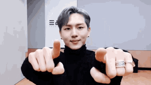a young man wearing a black turtleneck sweater is pointing at the camera with his fingers .