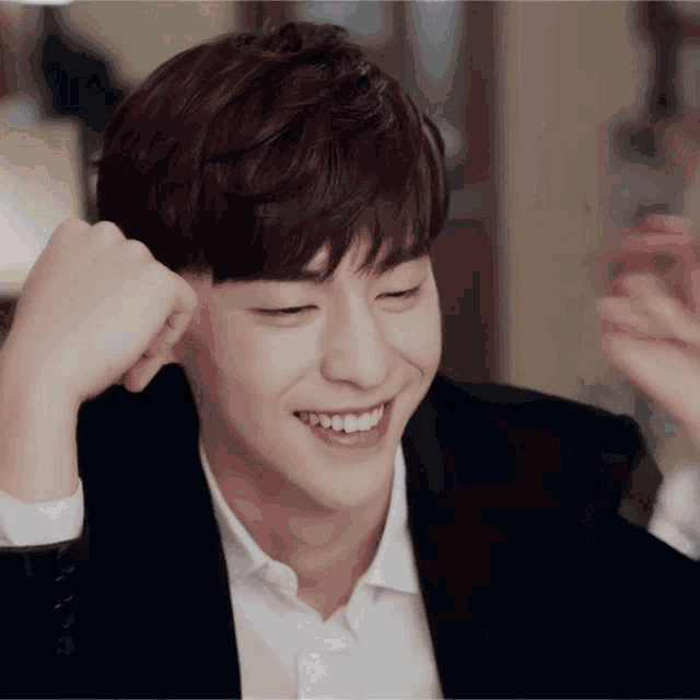 a man in a suit and white shirt is smiling with his hand on his ear