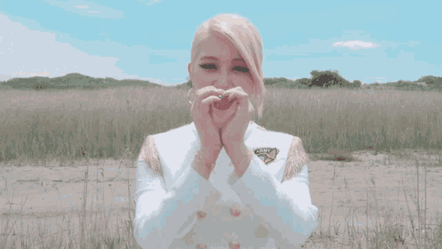 a woman making a heart shape with her hands while wearing a white jacket with the word army on it