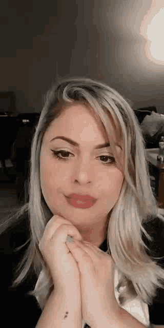a woman with blonde hair and a tattoo on her wrist is looking at the camera .