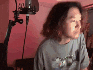 a man with long hair is singing into a microphone in a room .
