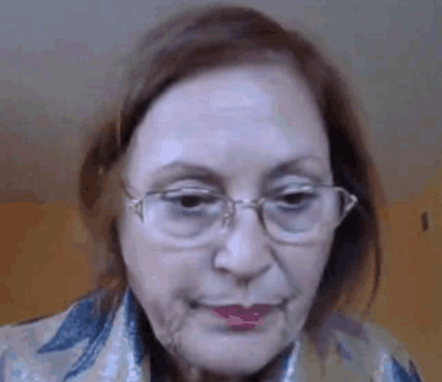 an elderly woman wearing glasses and a scarf looks at the camera