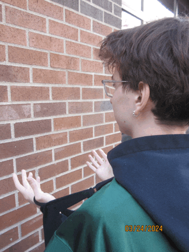 a person standing in front of a brick wall with the date 03/24 2024