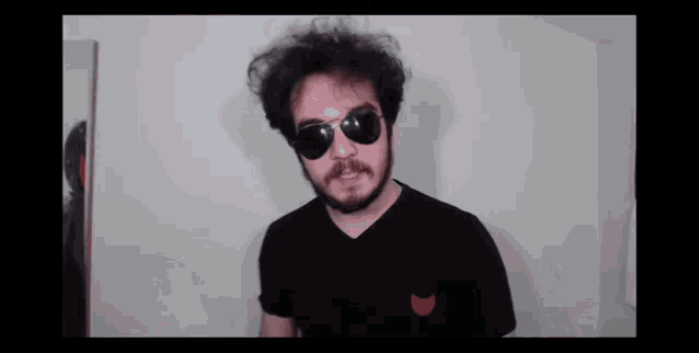 a man with a beard wears sunglasses and a black shirt